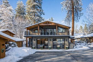 Une cabane en bois à deux étages, dotée d’un balcon et entourée d’arbres couverts de neige.