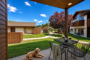 Eine Terrasse mit Tisch und Stühlen, einem Hund und einem Haus im Hintergrund.