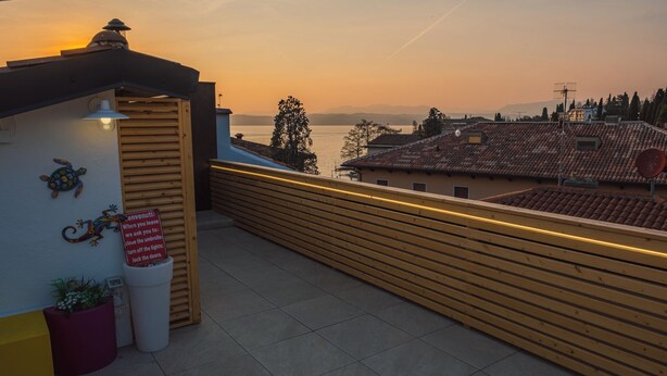 A rooftop terrace with a view of the sunset, a wooden railing, and a sign with instructions for guests. - Sunset Sirmione Lake View (Sirmione)