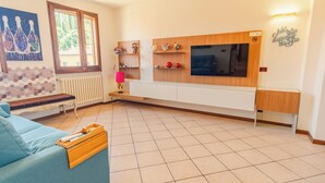 A modern living room with a sofa, a TV mounted on a wooden wall, a bench, and decorative items on shelves. - Sunset Sirmione Lake View (Sirmione)