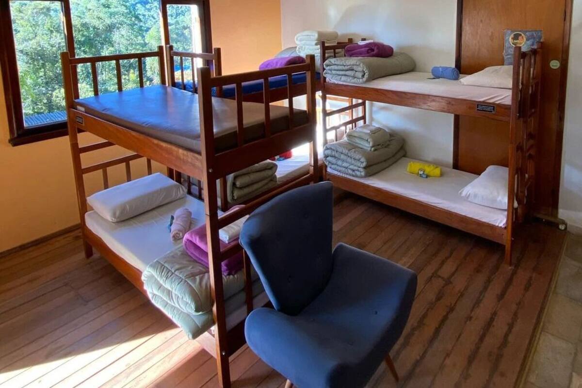 Habitación con literas, una silla azul, piso de madera y ventana con vista a árboles.