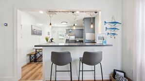 Een moderne keuken met een centraal eiland, twee barkrukken, hangende lampen en decoratieve muurkunst met vismotieven.