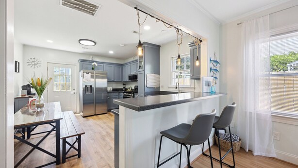 Een moderne keuken met grijze kastjes, een centraal eiland en barstoelen.