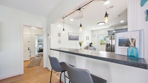 Een moderne keuken met een zwart aanrecht, twee barkrukken, hangende pendantlampen en een koelkast.