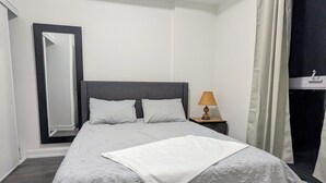 A neatly made bed with a white bedspread and two pillows, a bedside table with a lamp, and a large mirror on the wall.