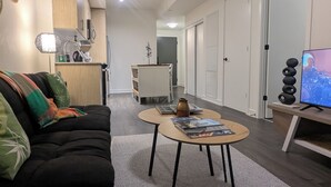 A modern living room with a black sofa, a coffee table, a TV, and a kitchen area in the background.