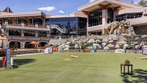 Ein Hotel im modernen Architekturstil, mit einer großen Glasfassade, einer Sitzgelegenheit im Freien mit orangefarbenen Sonnenschirmen und einem angelegten Garten mit einem kleinen Wasserfall.