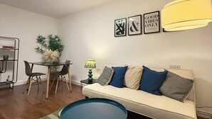 A modern living room with a sofa, a round coffee table, and a dining area with chairs and a table. There are framed pictures on the wall and a lamp on the side table. - Spacious apartment in central London - 10-15 minutes from major attractions! (London)