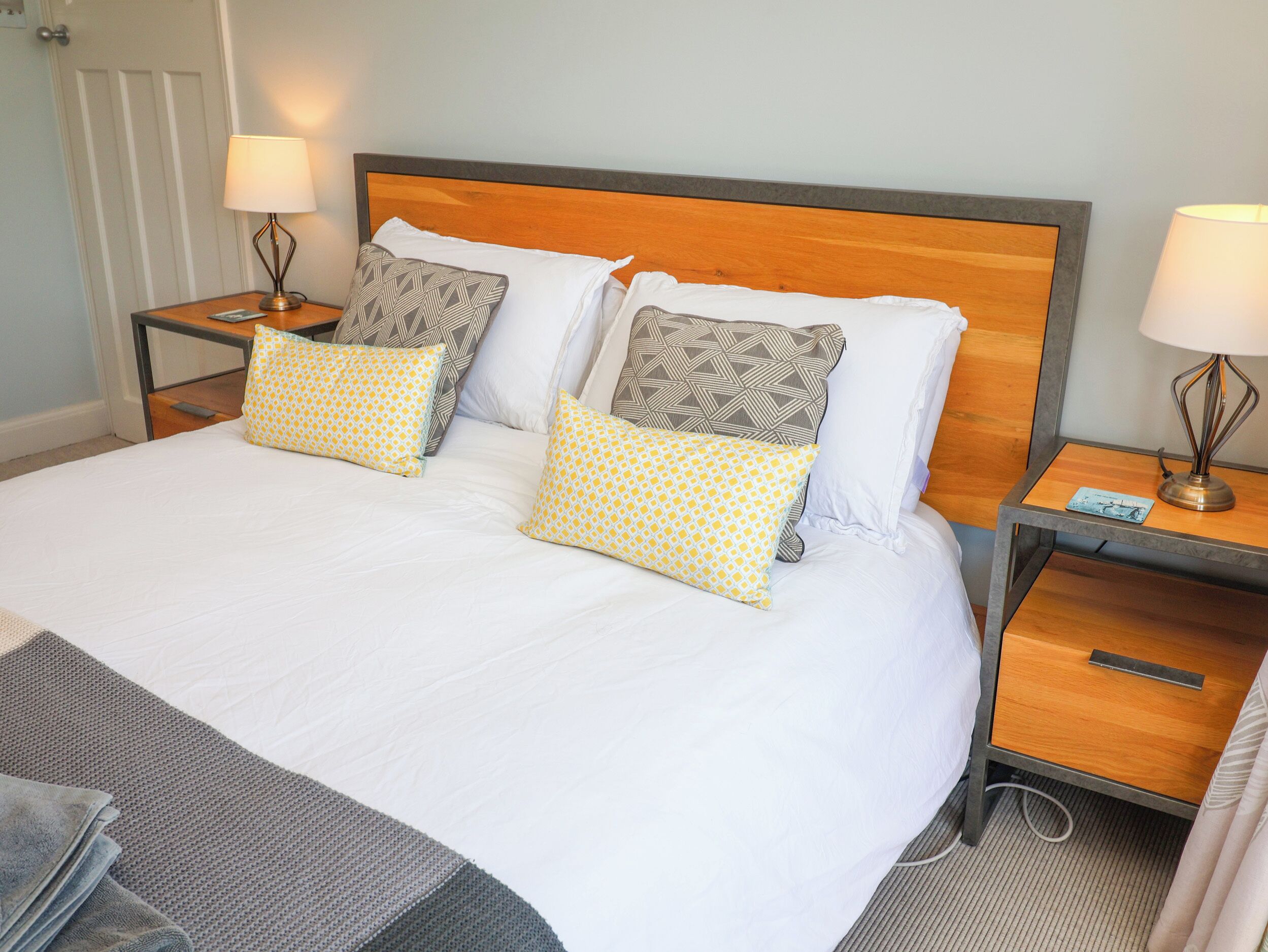 A neatly made bed with white bedding and patterned pillows, flanked by bedside tables with lamps and a small drawer.