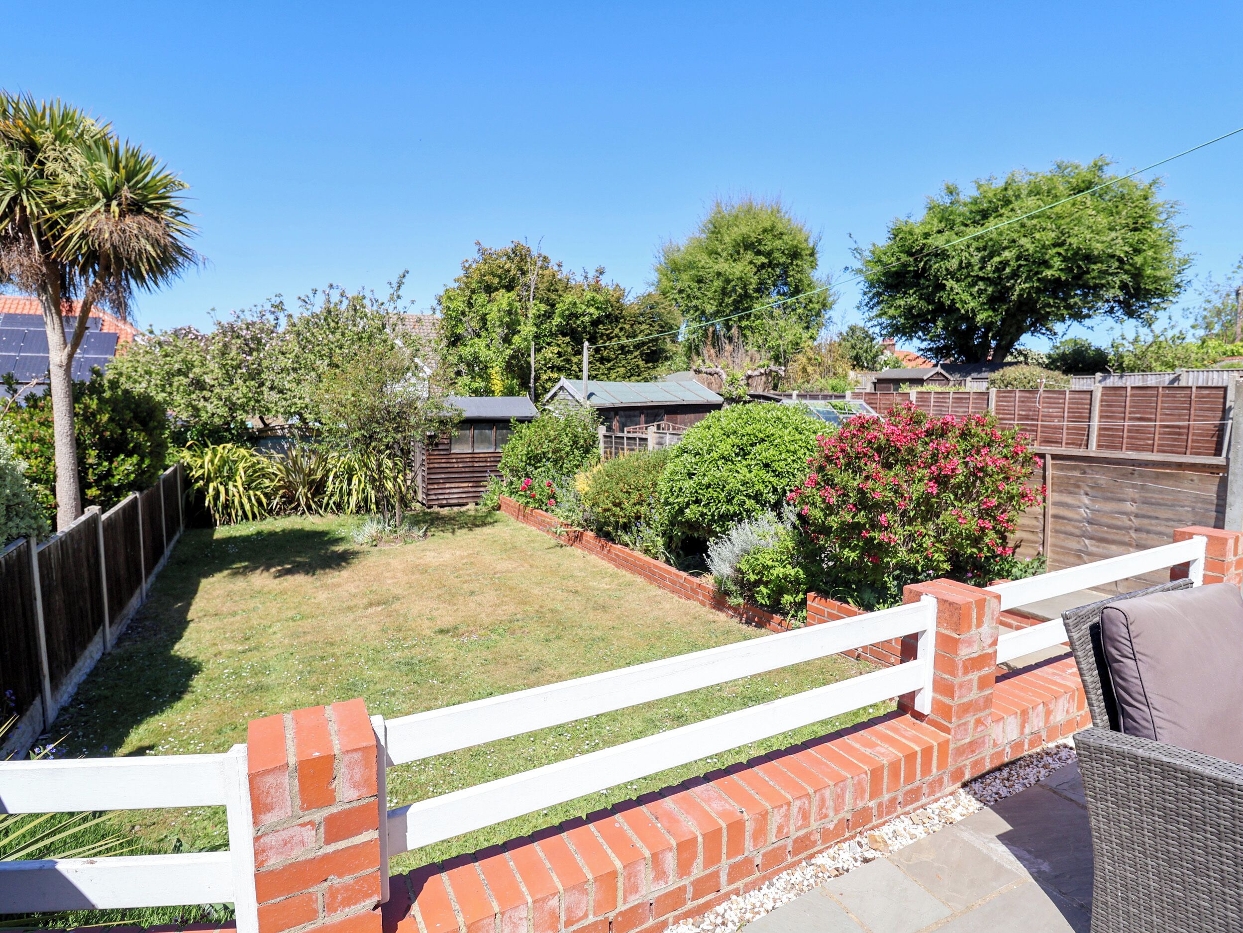 A backyard with a white fence, a brick wall, and various plants and trees.