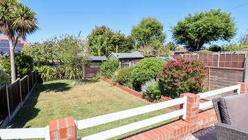 A backyard with a white fence, a brick wall, and various plants and trees.