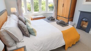 A neatly made bed with pillows, a bedside table with towels, a wardrobe, and a fireplace. - The Waverley (Reydon)