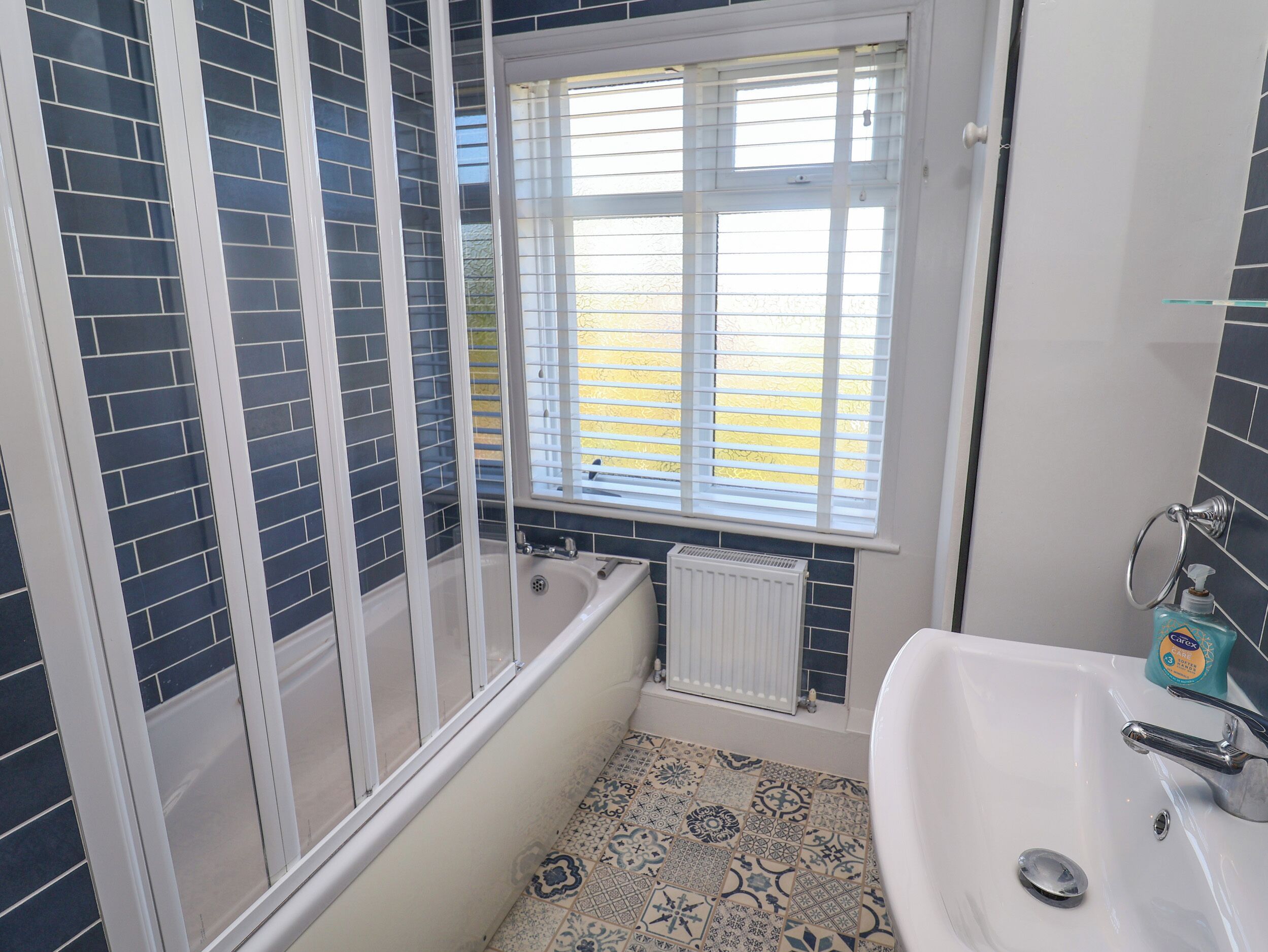 A bathroom with a bathtub, a sink, and a window with blinds.