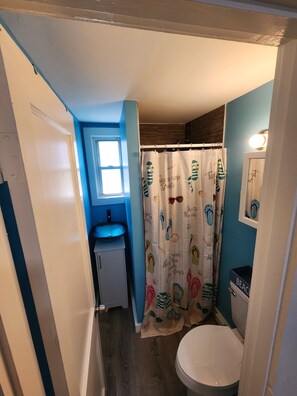 A bathroom with a toilet, a sink, and a shower curtain with a beach theme. - G St Inn Unit 3 Charming 1-bedroom apartment in welcoming Hampton with AC, WiFi (Hampton)