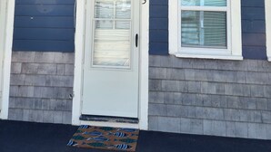 A house with a dark blue exterior, a white door with a glass panel, and a small window with shutters.