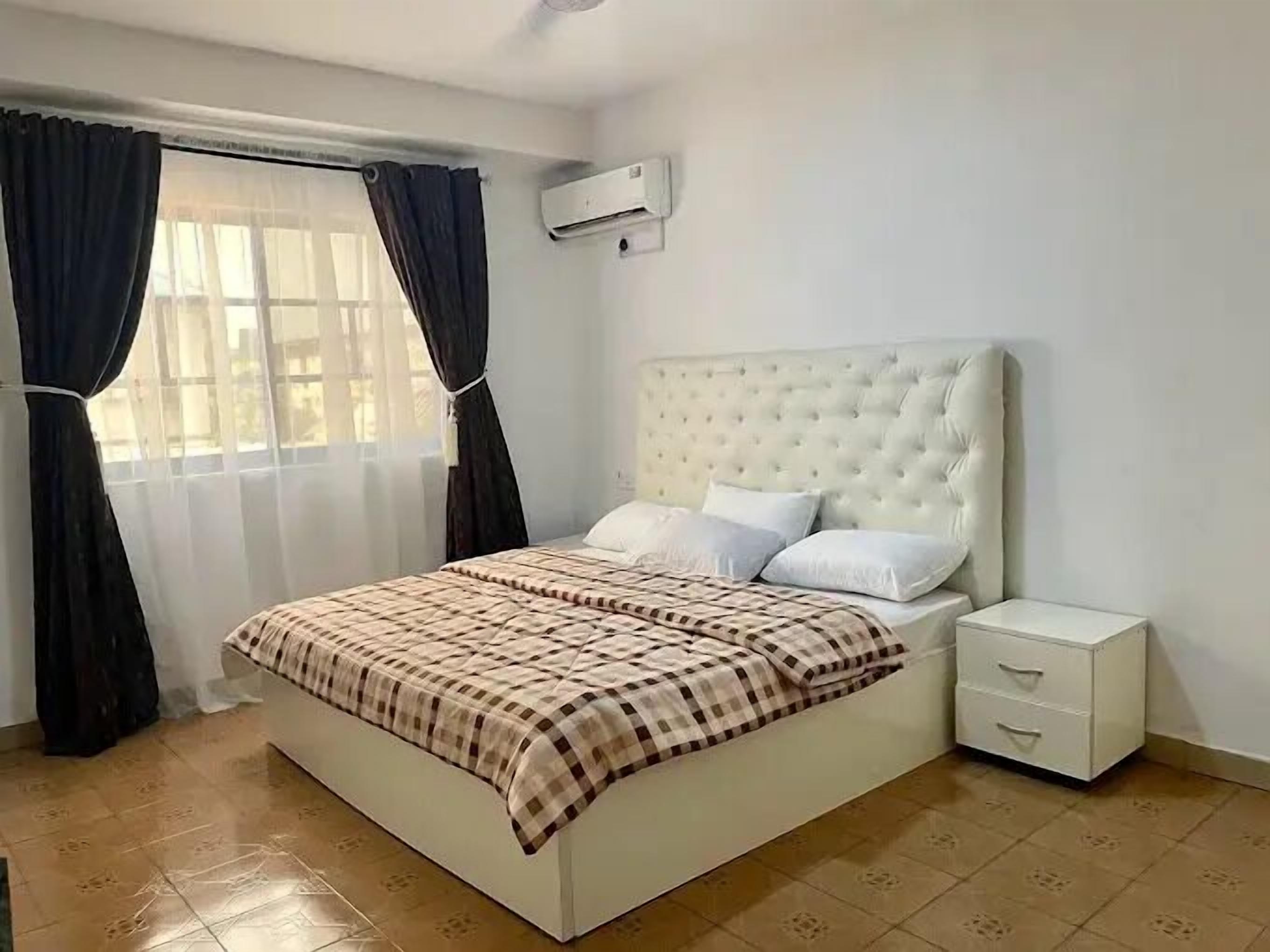 Een slaapkamer met een groot bed, een nachtkastje en een raam met gordijnen.