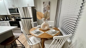 A modern kitchen with white cabinetry, a stainless steel refrigerator, and a dining area with a wooden table and white chairs. - 2 king beds -2nd fl walk 2 beach #5 (norfolk)