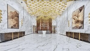 A spacious lobby with marble floors and walls, a central reception desk, and large floral wall art.