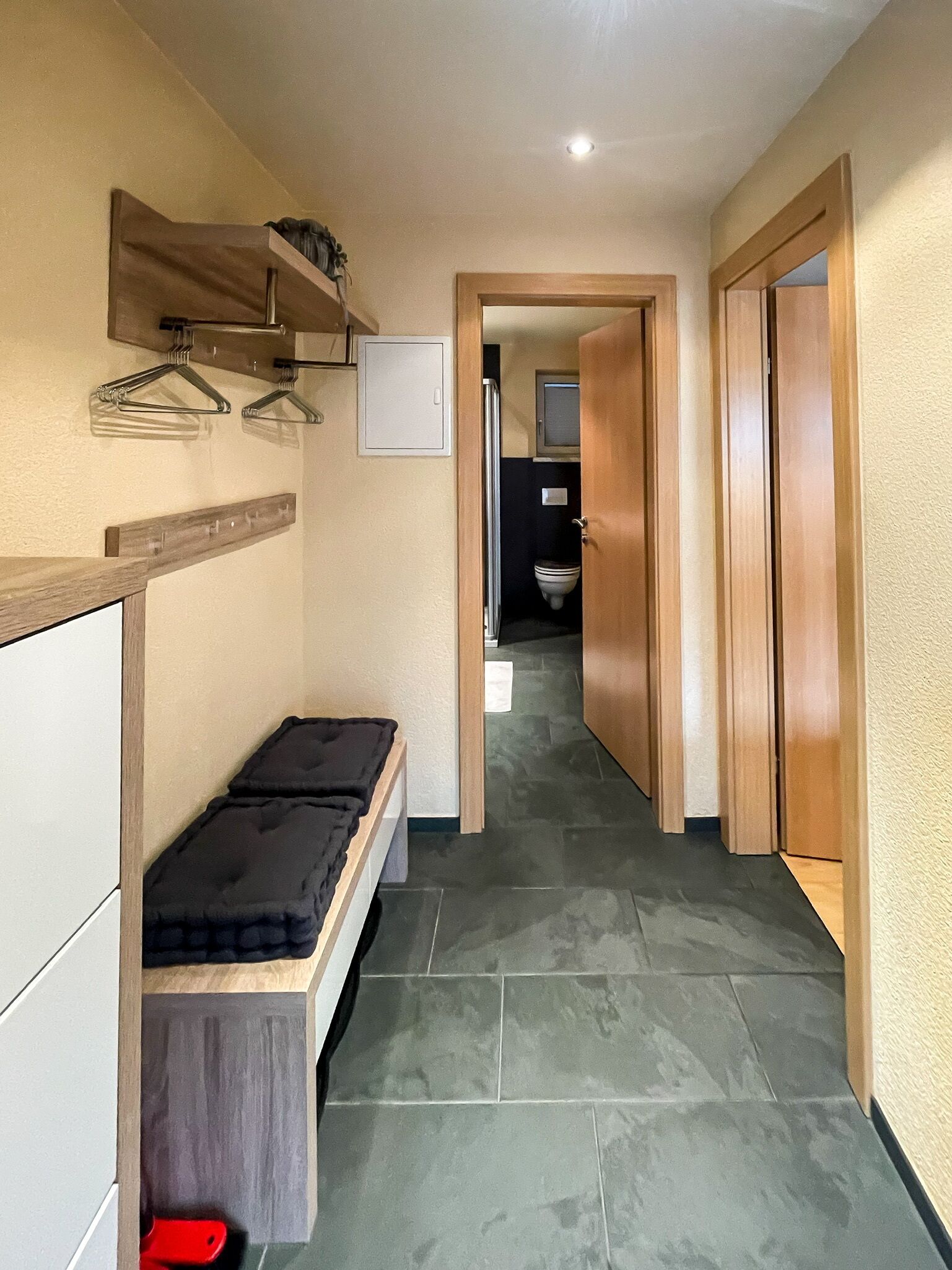A hallway with a bench, wooden doors, and a tiled floor.