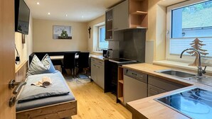 A compact living space with a kitchenette, a bed with a towel, a dining area, and a window with a view. - Apartment Waldnah (Fließ)