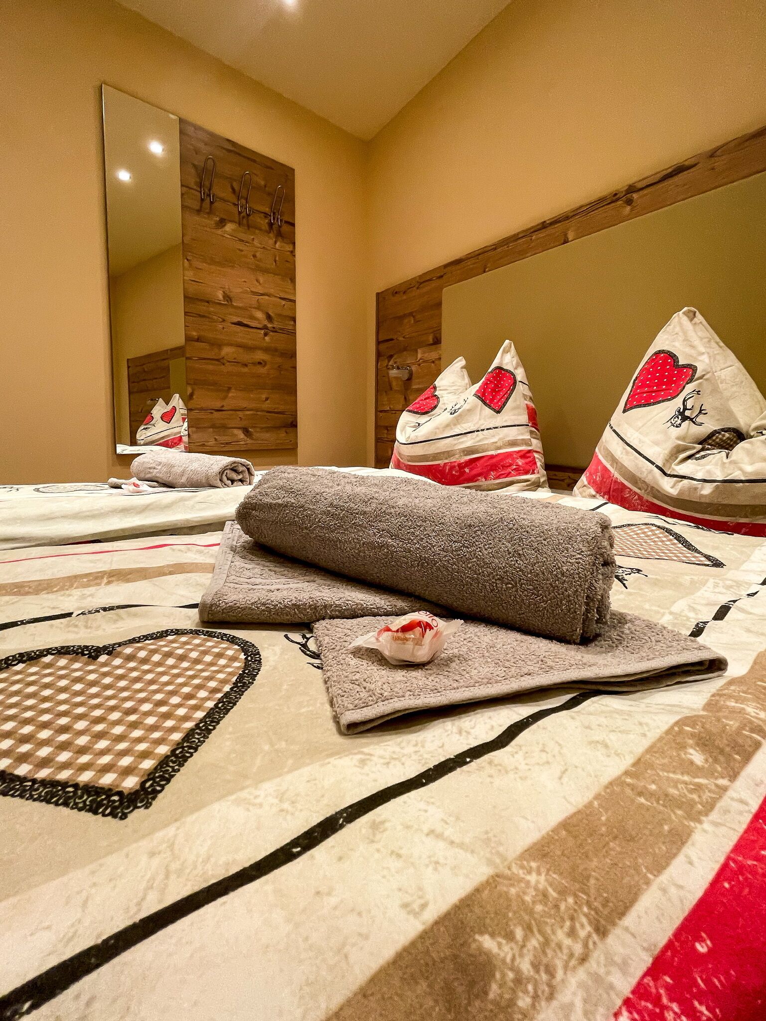 A hotel room with a large bed, a wooden headboard, a mirror, and decorative pillows with heart designs.