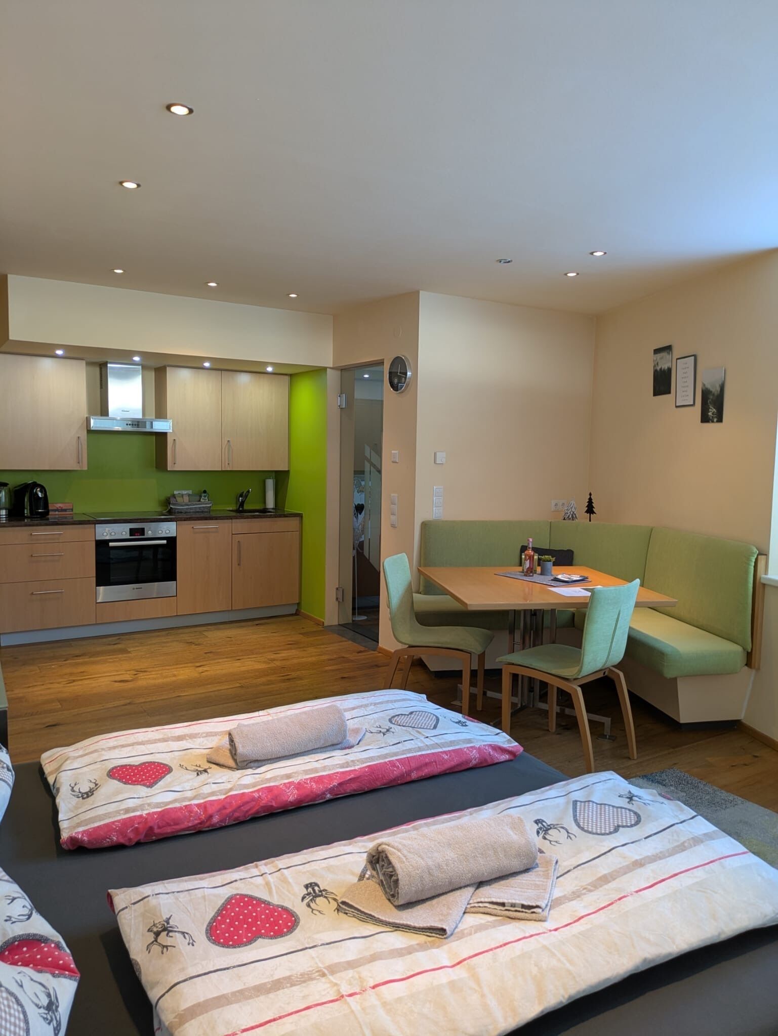 A compact living space with a kitchenette, a dining area with a green booth, and a bed with patterned bedding.