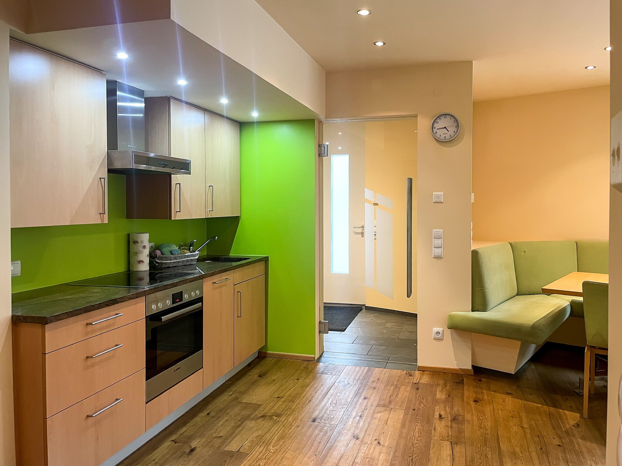 A modern kitchen with wooden cabinets, a built-in oven, and a green accent wall.