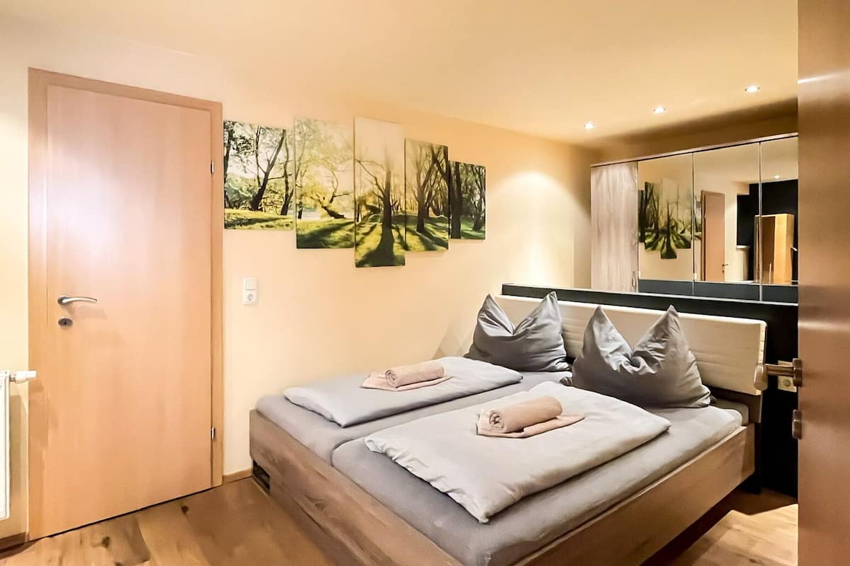 A bedroom with a bed, a door, a wall-mounted artwork, and a mirror.