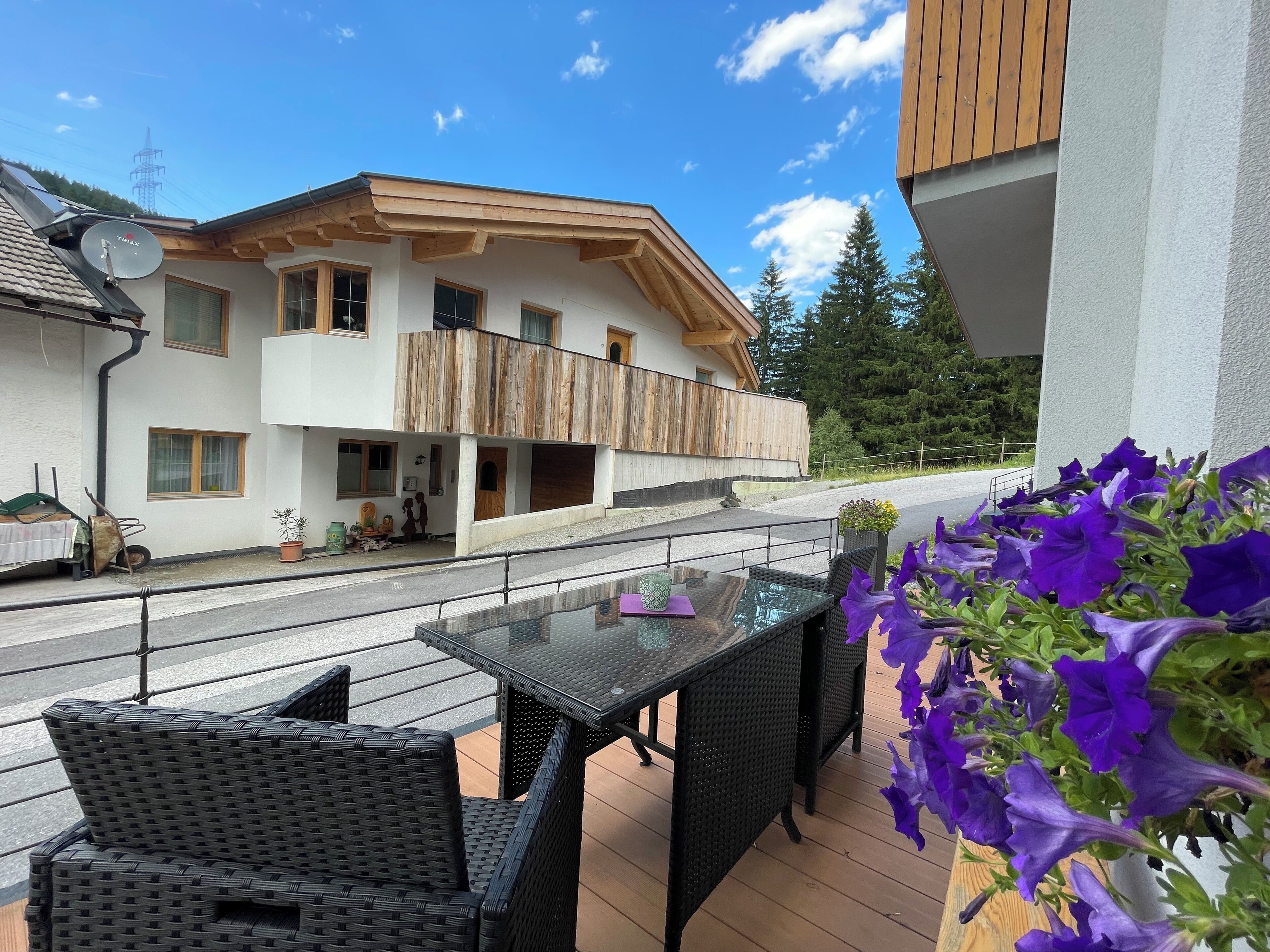 A balcony with wicker furniture, a table, and purple flowers.