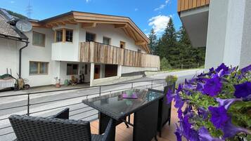 A balcony with wicker furniture, a table, and purple flowers.