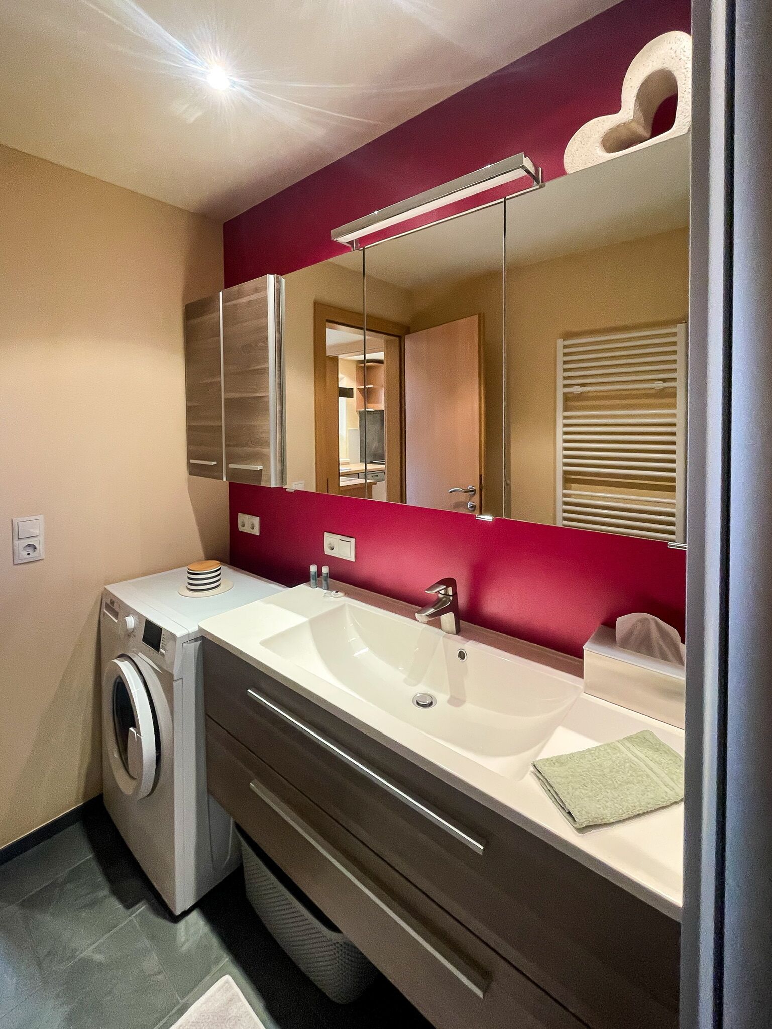 A modern bathroom with a dual sink vanity, a built-in washing machine, and a large mirror.