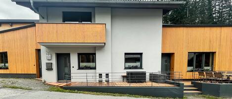 A modern two-story building with a flat roof, large windows, and a balcony.