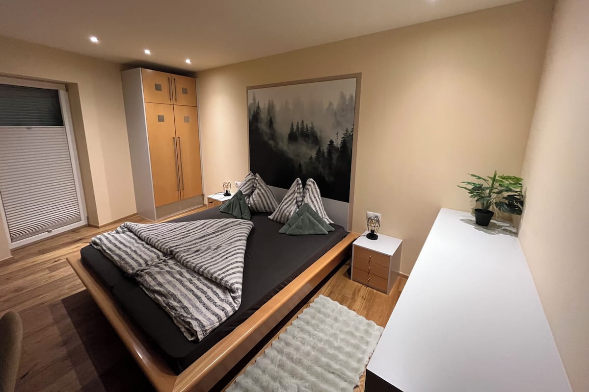 A modern bedroom with a bed, bedside table, and a large painting of a forest.