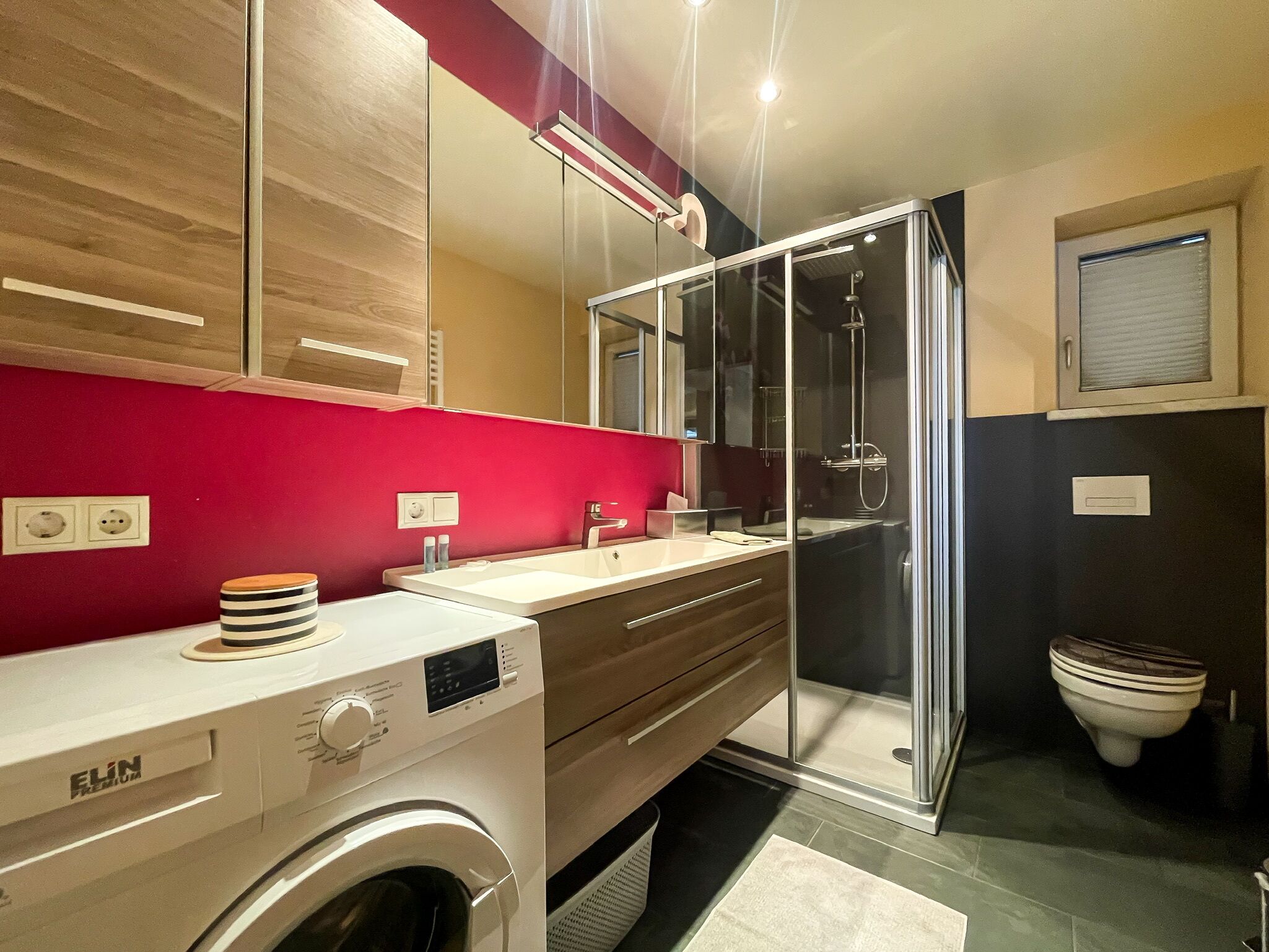 A modern bathroom with a washing machine, a glass shower enclosure, and a toilet.