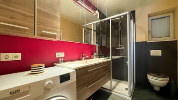 A modern bathroom with a washing machine, a glass shower enclosure, and a toilet.
