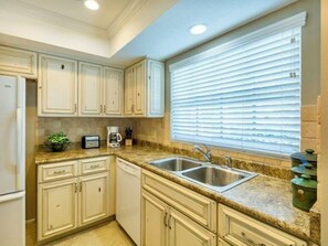 A kitchen with white cabinets, a granite countertop, a double sink, and a window with blinds.