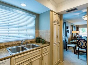 A kitchen with a double sink, cabinets, and a window with blinds.