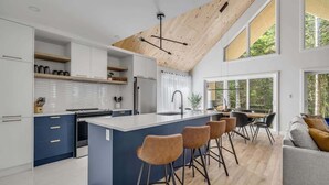 Une cuisine moderne dotée d’un îlot central, de meubles blancs et d’un plafond en pente avec des poutres apparentes.