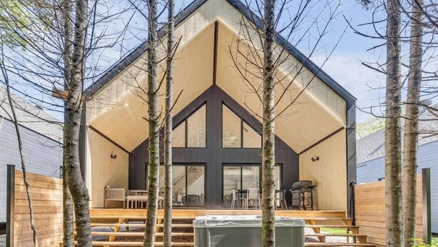 Une maison moderne avec un toit triangulaire, de grandes fenêtres et une terrasse en bois.