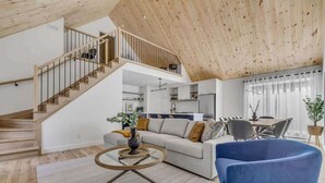 Un vaste espace de vie comprenant un escalier en bois, un canapé, une table basse et un coin repas.