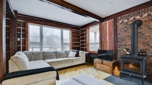 Un salon confortable avec un canapé, un téléviseur, une cheminée et de grandes fenêtres.