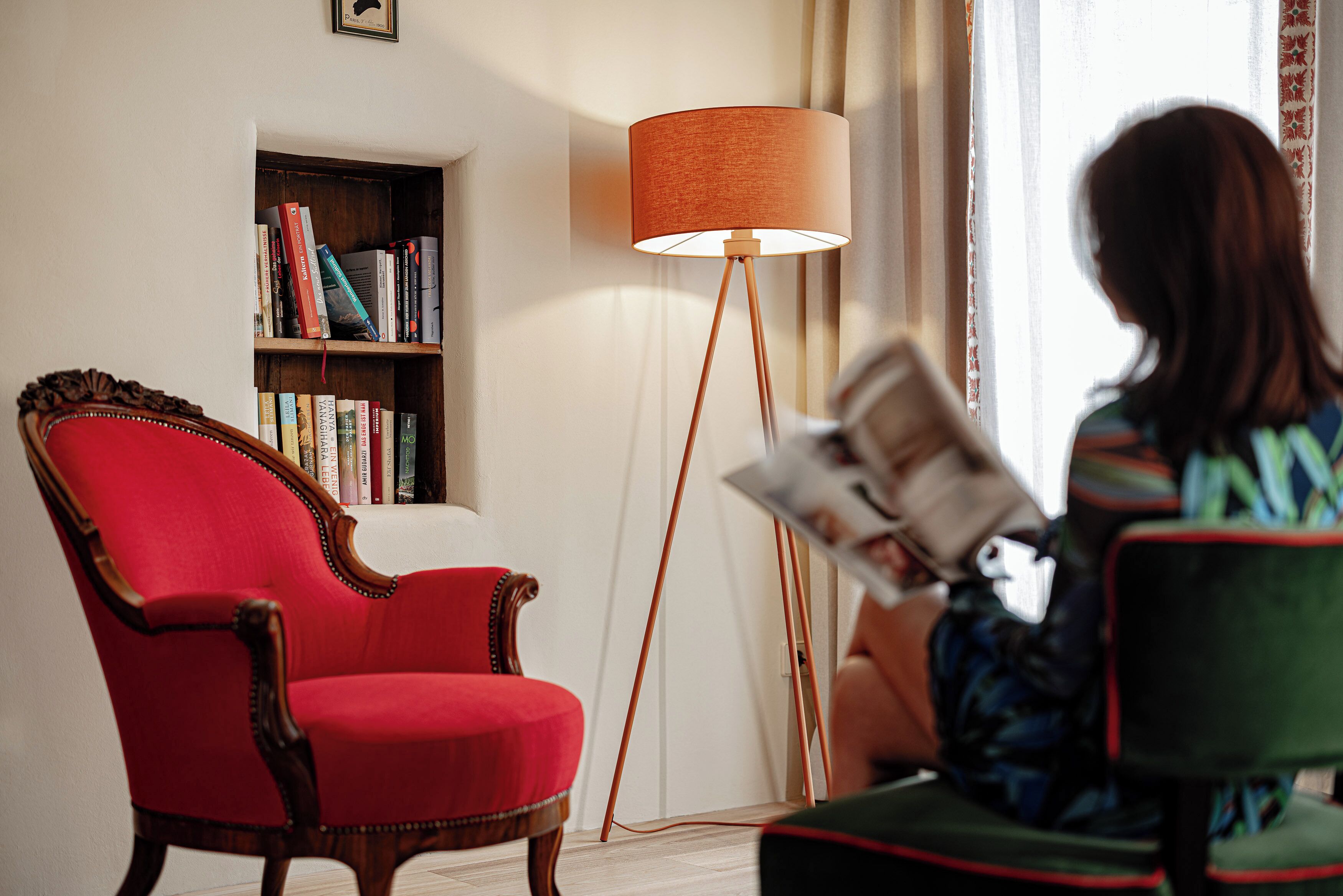 Una habitación con un sillón rojo, una lámpara de pie y una estantería.