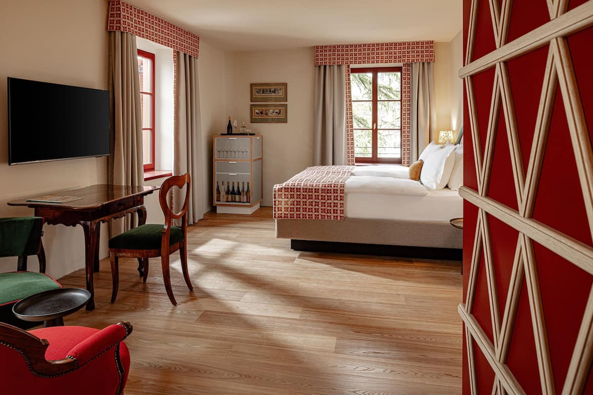 A hotel room with a bed, a desk with a chair, a television, and a wardrobe.