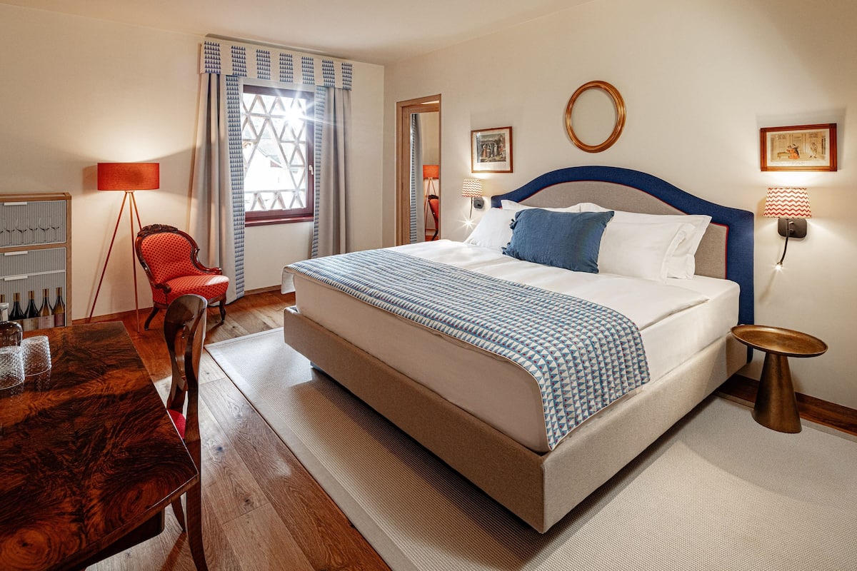A neatly arranged hotel room with a large bed, a wooden dining table, and a red armchair.