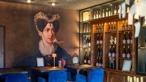 A bar area with a large portrait on the wall, wooden shelves with bottles, and blue chairs. - Castel Sallegg Suites Adults only (Caldaro Sulla Strada del Vino)