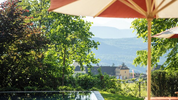 An infinity pool with wooden lounge chairs and a table, surrounded by lush greenery and a view of distant mountains. - Castel Sallegg Suites Adults only (Caldaro Sulla Strada del Vino)
