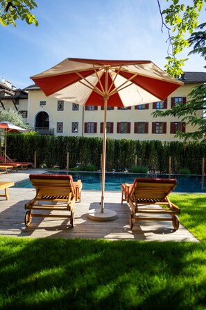 Zona de piscina amb gandules de fusta i un gran parasol.