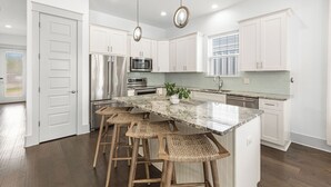 A modern kitchen with white cabinets, stainless steel appliances, a marble countertop, and a central island with bar stools.