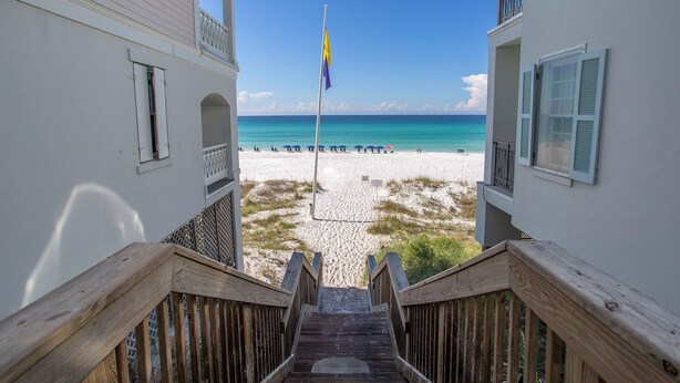 A wooden staircase leading to a beach with a flagpole and umbrellas.