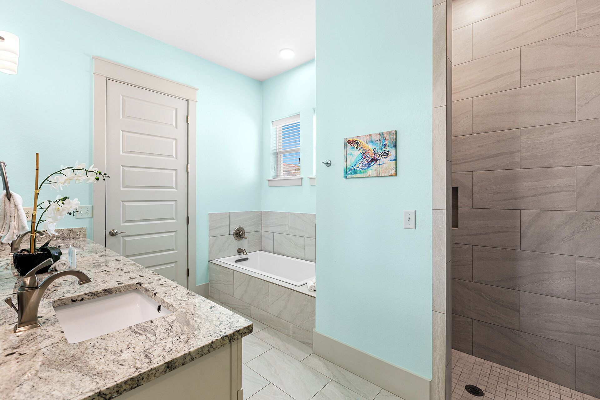 A bathroom with a white door, a sink with a marble countertop, a bathtub, and a shower area with tiled walls.